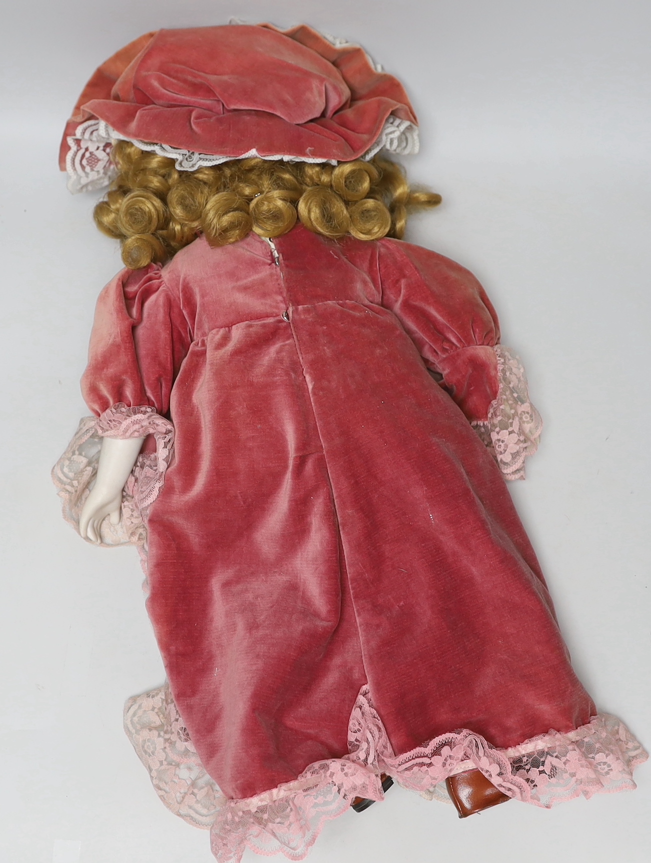 A doll with bisque face and hands, wearing a velvet dress and bonnet, 66cm high